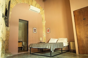 Un dormitorio con cama, puerta de madera, unidad de aire acondicionado y espejo.