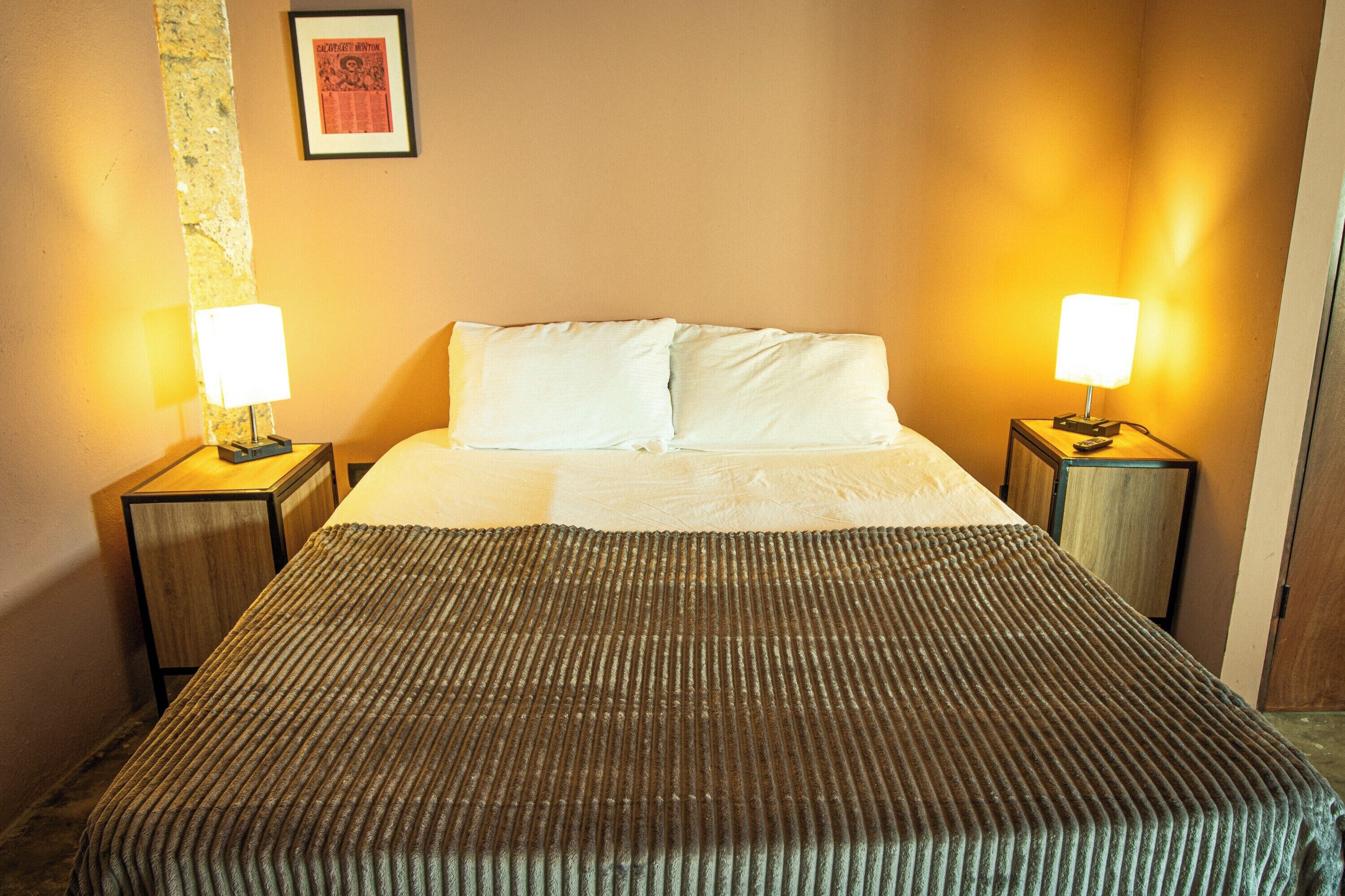 Una habitación de hotel con una cama, dos lámparas de noche y un cuadro en la pared.