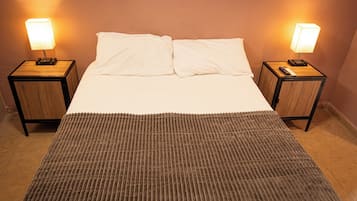 Cama doble con dos mesitas de noche, cada una con una lámpara, en una habitación con un tapete marrón texturizado.