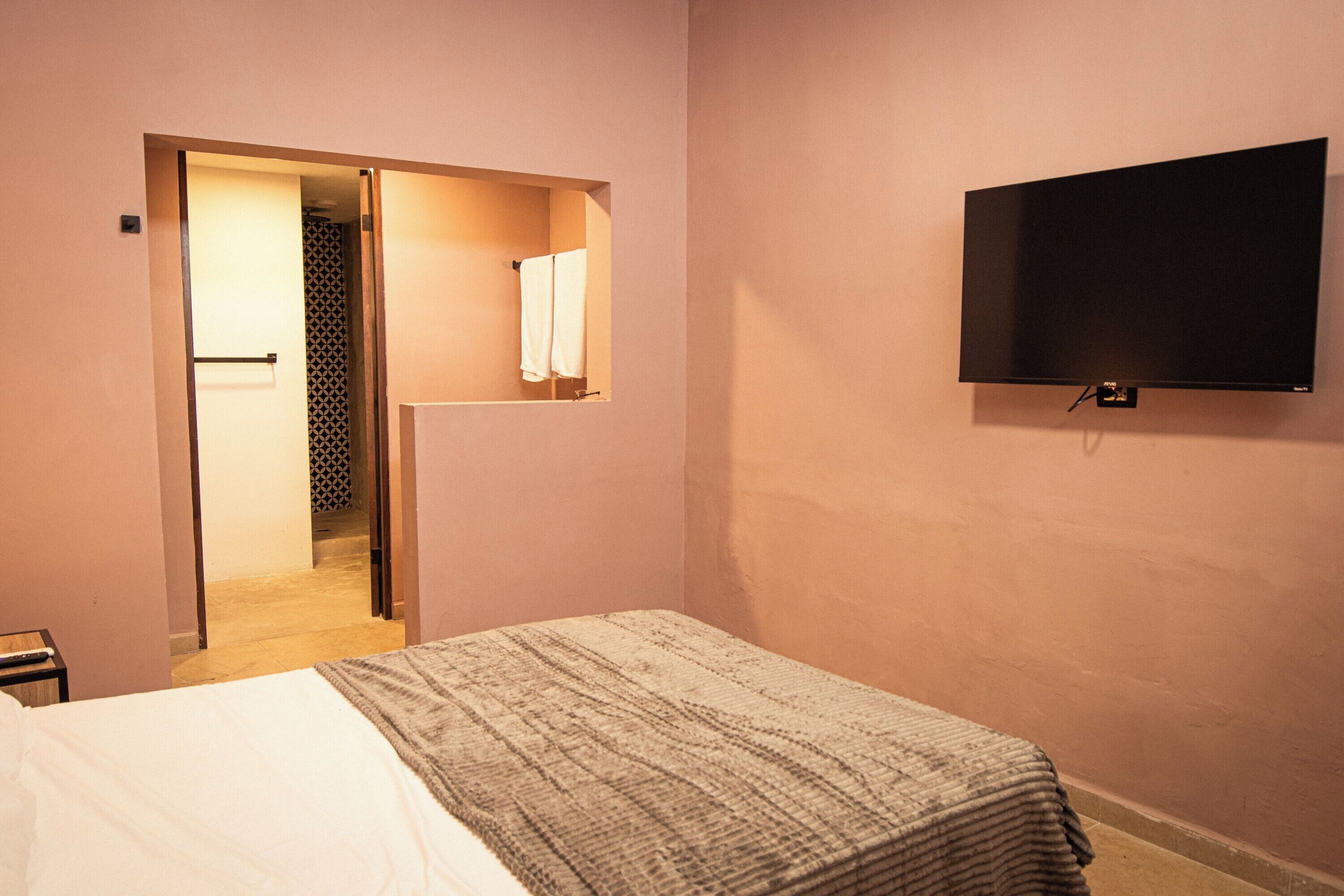Habitación de hotel con cama, televisión montada en la pared y puerta abierta a un baño.