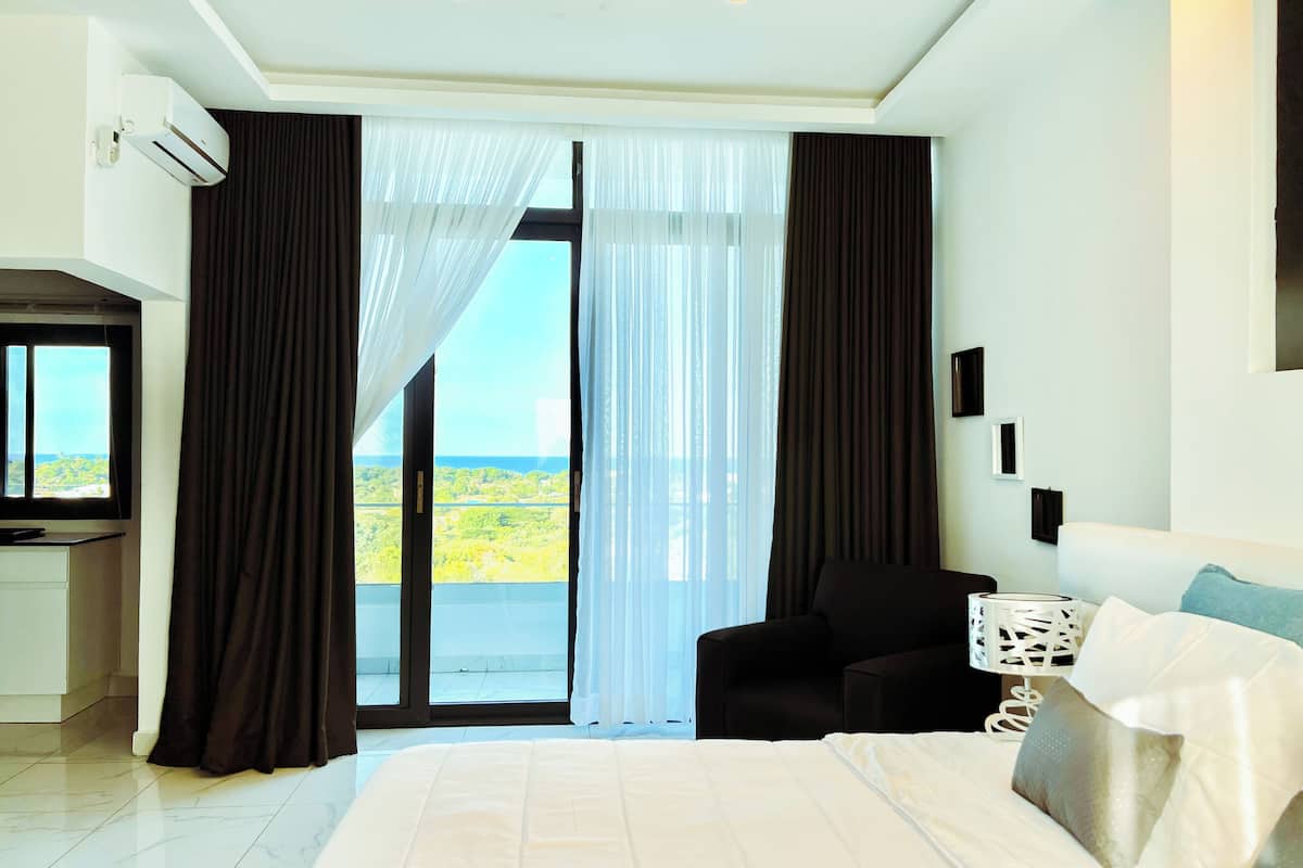 Habitación de hotel con una cama grande, un escritorio y una silla. Se ve una ventana con cortinas y vistas a zonas verdes.