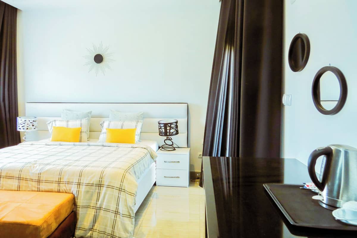 Habitación de hotel con cama, mesitas de noche, escritorio con tetera y espejo en la pared.