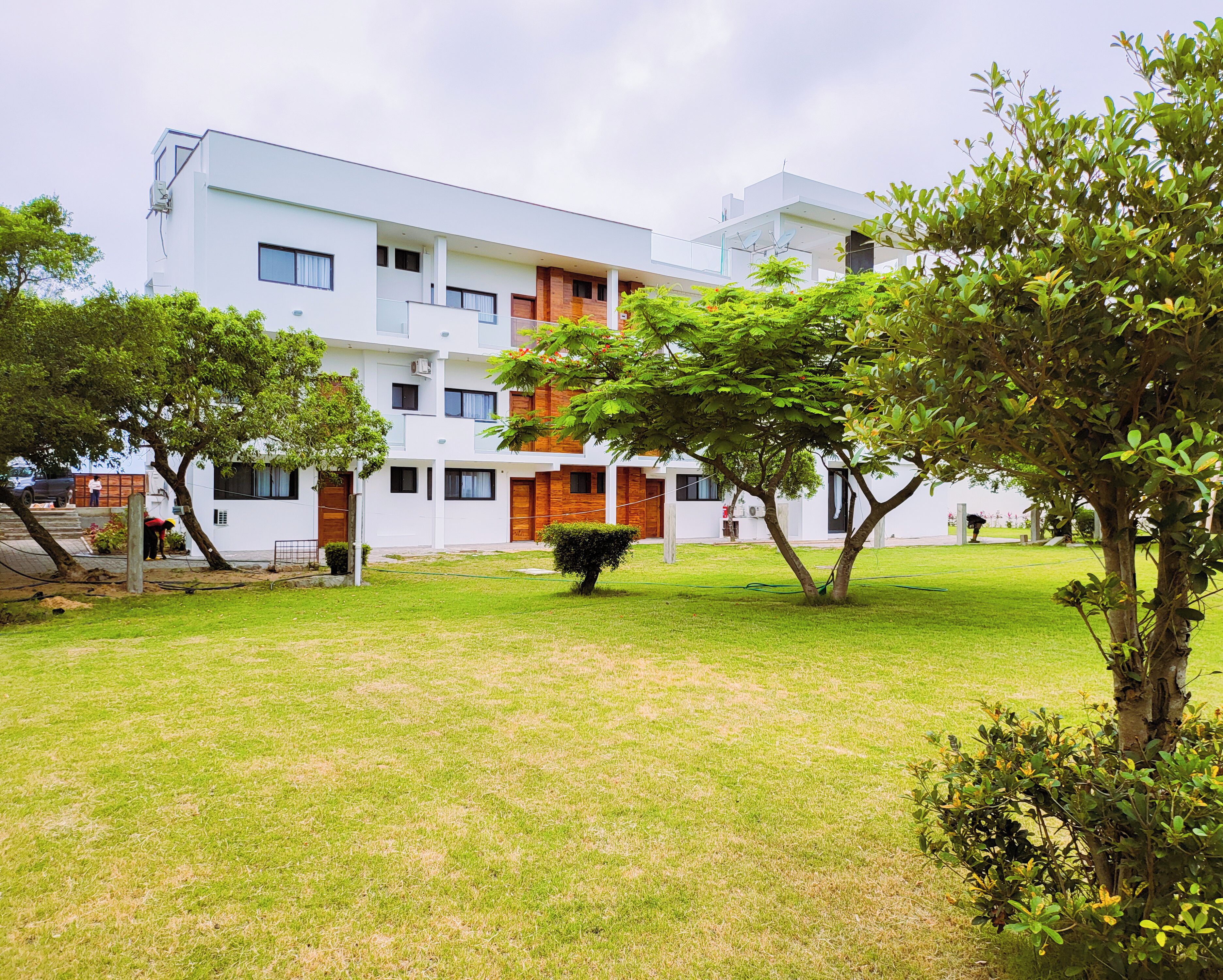 A modern multi-story building with a flat roof, surrounded by a well-maintained grassy area with trees and shrubs.