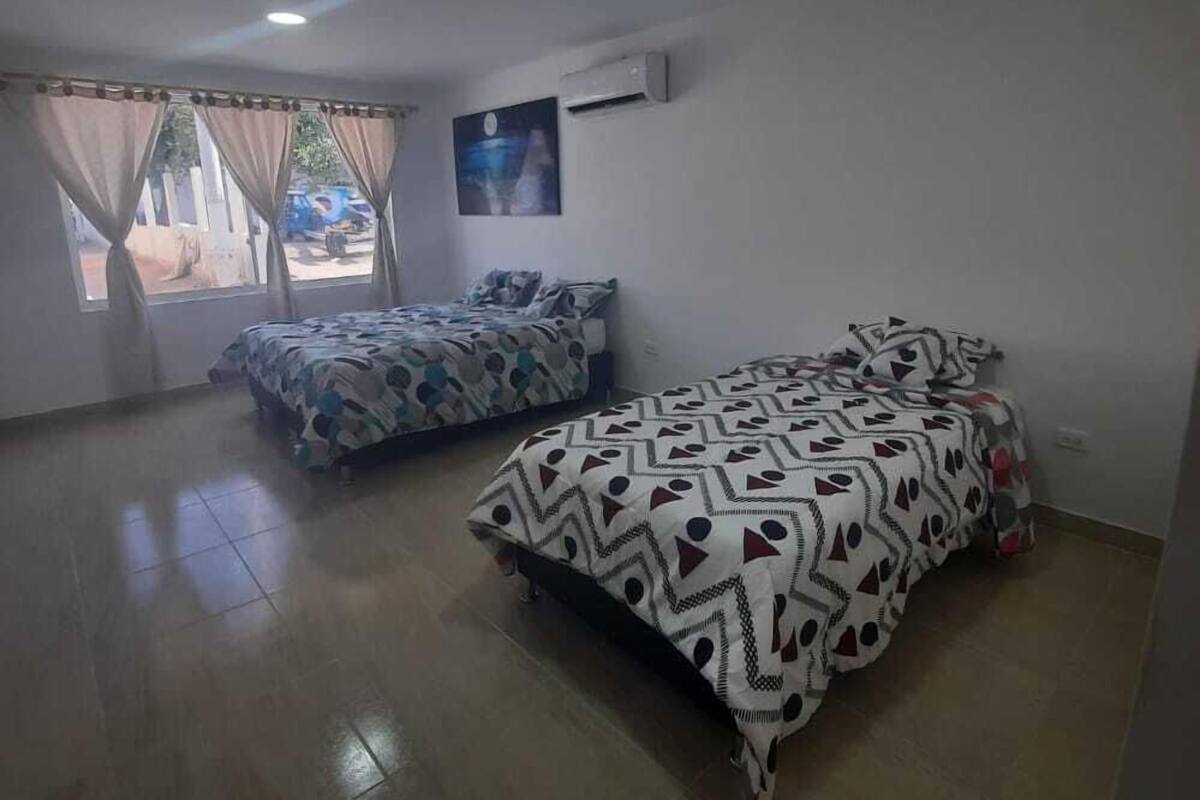 Una habitación con dos camas, una ventana con cortinas, un aire acondicionado de pared y un cuadro.