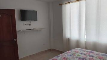 A bedroom with a bed, a TV mounted on the wall, a door, and a window with curtains.