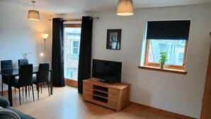 Ett modernt vardagsrum med en soffa, en tv på ett träställ, ett matbord med stolar och ett fönster med en växt.