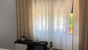 Un dormitorio moderno con cama, sofá, una mesita con objetos decorativos y ventana con cortinas translúcidas.