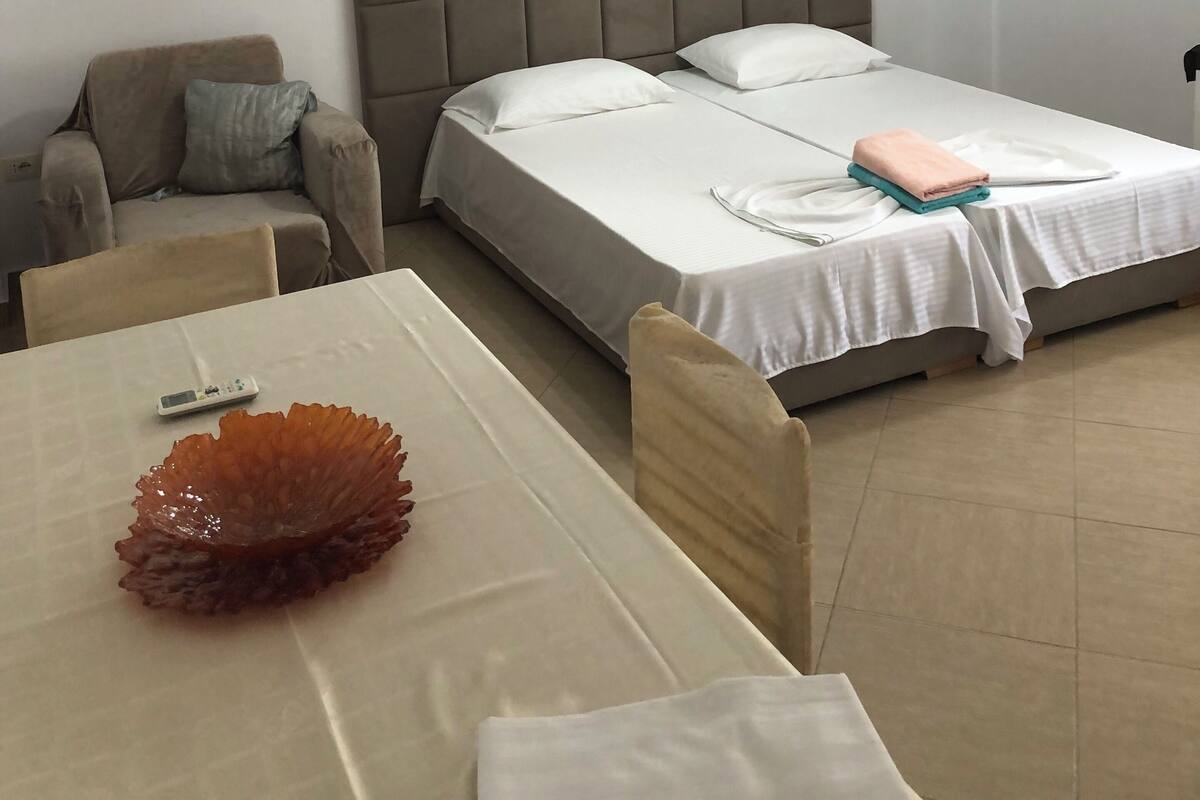 A hotel room with a bed, a sofa, a dining table, and a ceiling fan.