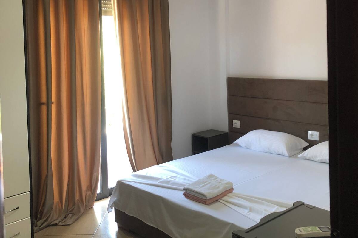 A hotel room with a bed, bedside table, and a lamp.