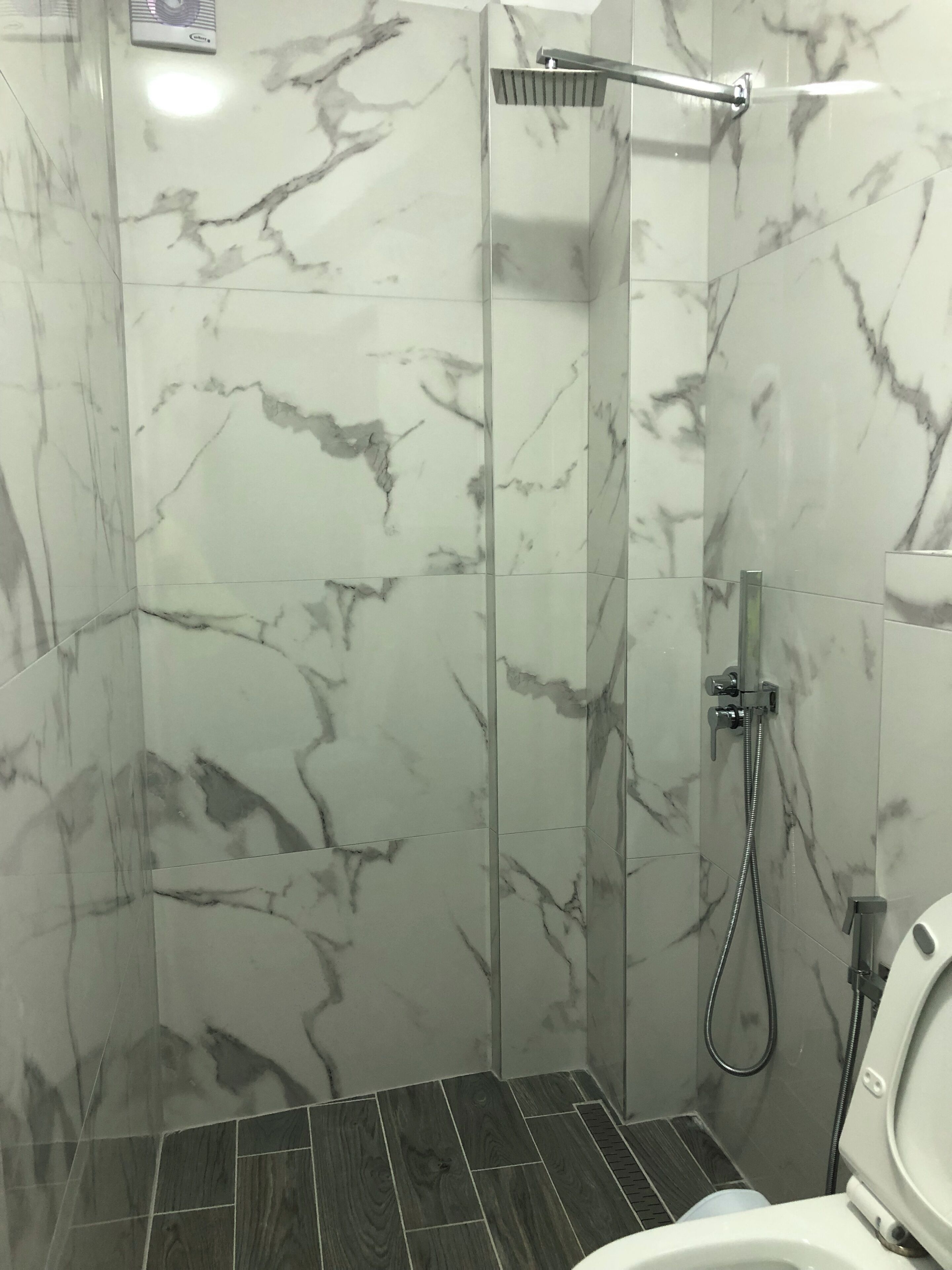 A bathroom with a shower, toilet, and marble walls.