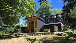 Une maison moderne à deux étages, dont le rez-de-chaussée présente une structure en bois évoquant un chalet, et dont l’étage supérieur est doté d’un balcon.