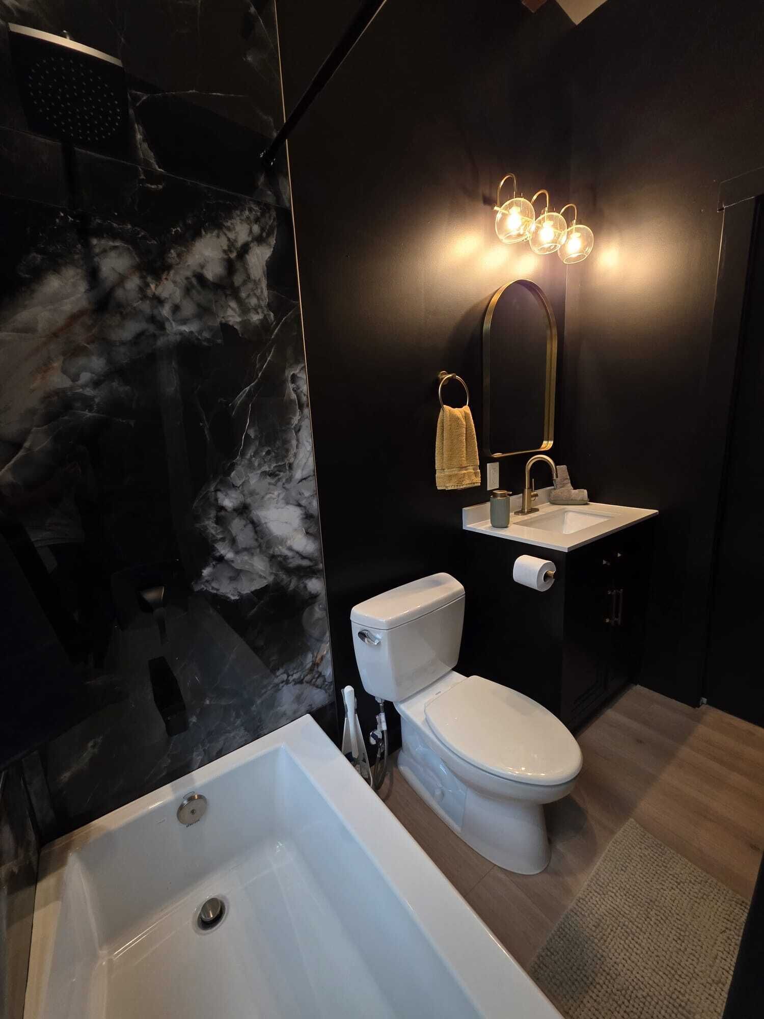 Une salle de bain moderne avec un mur en marbre, une baignoire, des toilettes et un lavabo agrémenté d’un miroir.
