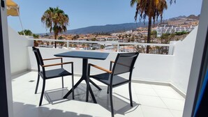 A balcony with a table and two chairs, overlooking a coastal town with palm trees and buildings. - Echeide: A cozy retreat in Costa Adeje with breathtaking views (Costa Adeje)