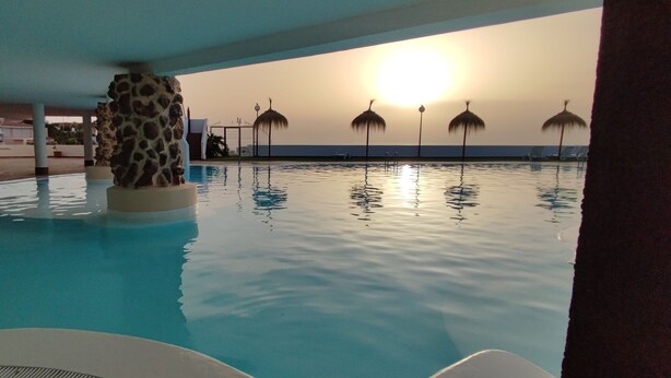 An indoor swimming pool with a sunset view, lounge chairs, and palm-shaped umbrellas. - Echeide: A cozy retreat in Costa Adeje with breathtaking views (Costa Adeje)