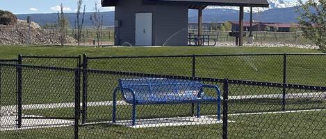 A fenced park area with a small pavilion, a blue bench, and a paved walkway.