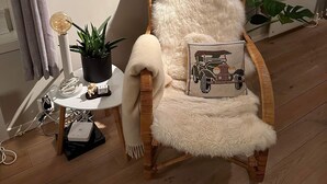 Een gezellige kamer met een zachte fauteuil, een klein bijzettafeltje met een lamp, een potplant en een lijst met een foto.
