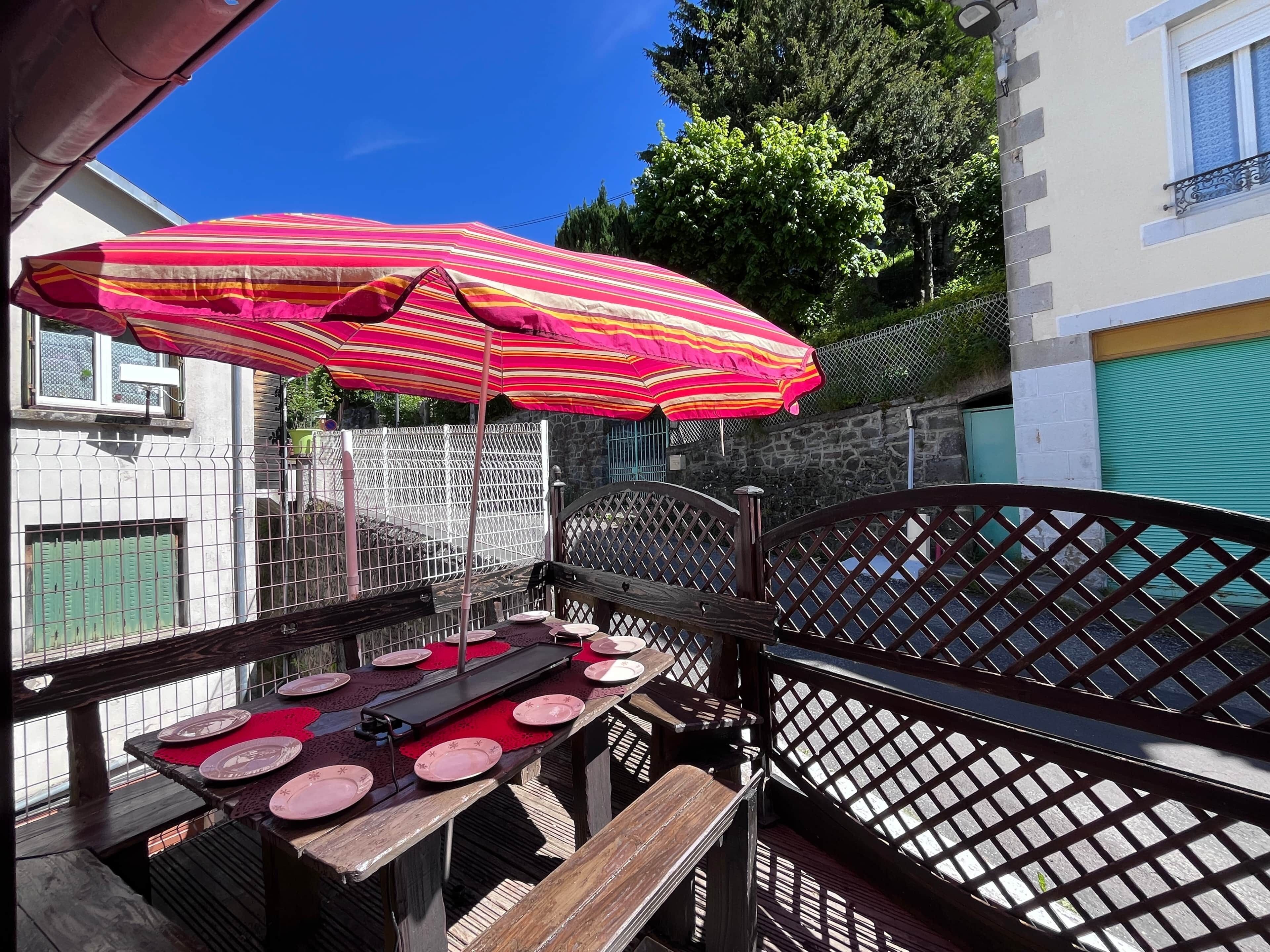 A patio with a table set for dining, a striped umbrella, and a metal fence.