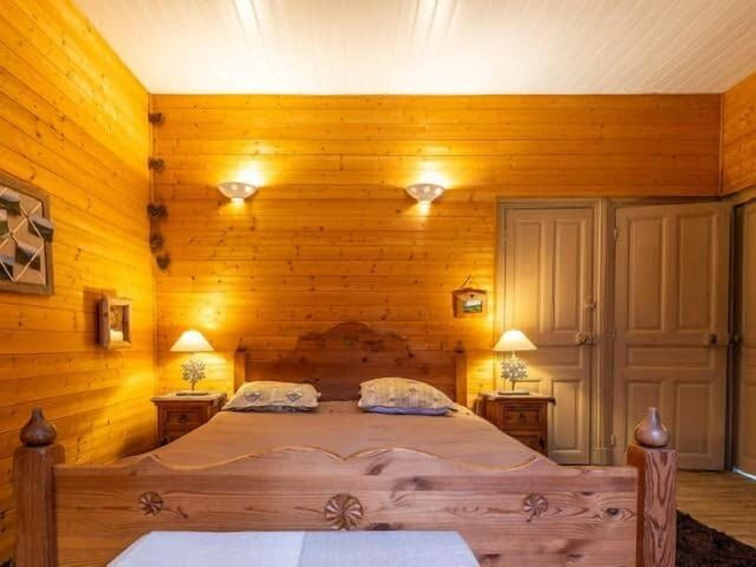 A wooden-paneled bedroom with a large bed, two bedside lamps, and a door.