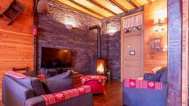 A cozy living room with a stone wall, a fireplace, and two sofas with red and blue cushions. - Holiday home 6 bedrooms, pool table, sauna, and foosbal (Le Mont-Dore)