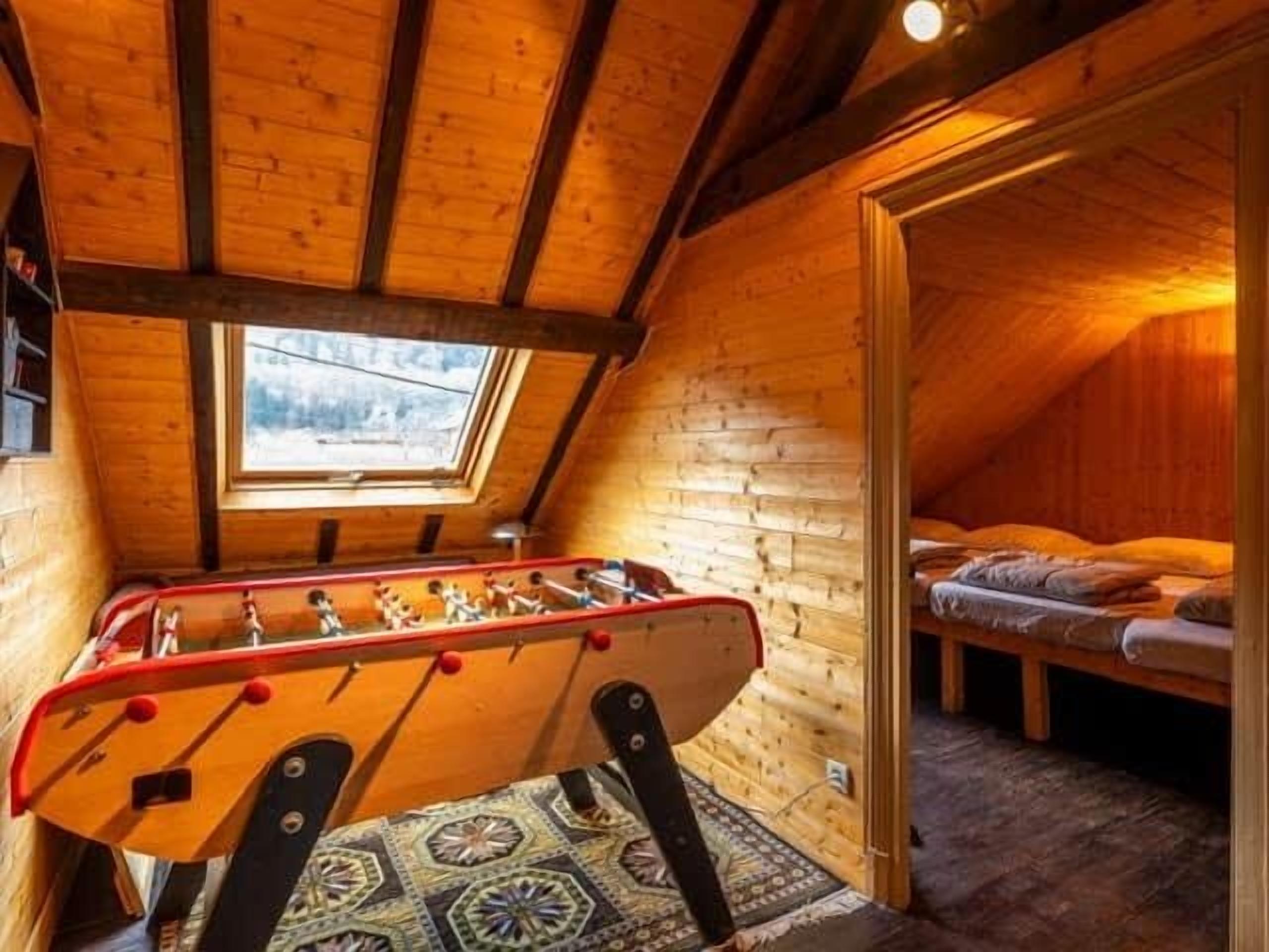 Une pièce mansardée chaleureuse avec des murs en bois, une table de baby-foot, un lit et une lucarne.