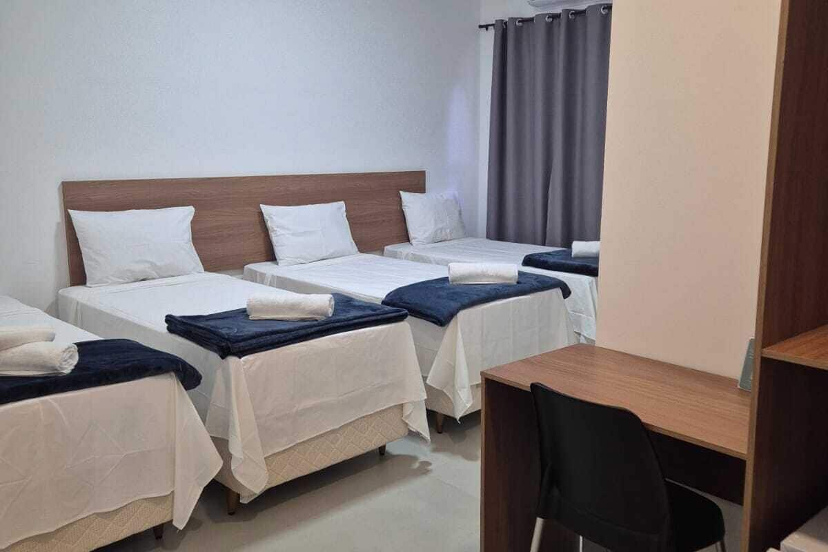 A hotel room with three single beds, a desk, and a chair.
