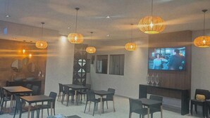 A restaurant with round tables, hanging wicker lamps, and a TV on the wall. - Hotel Villa Garden Janaúba (Janauba)