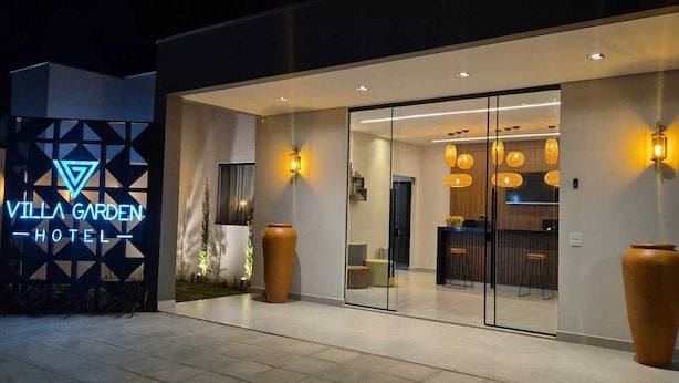 The exterior of Villa Garden Hotel with a modern design, featuring a glass entrance, warm lighting, and a prominent sign. - Hotel Villa Garden Janaúba (Janauba)