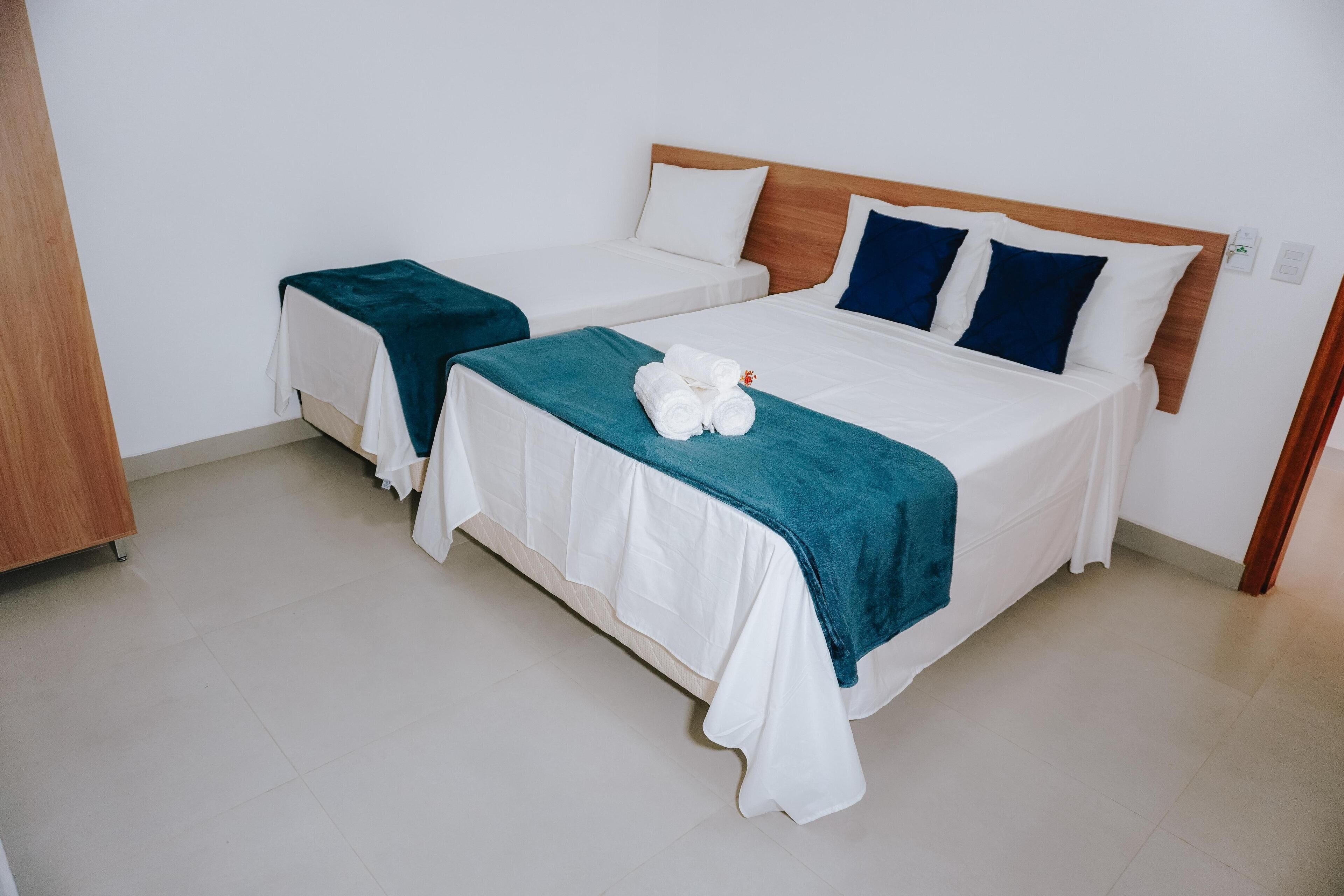 Habitación de hotel con dos camas individuales, cada una con cubrecama blanco y mantas turquesa.