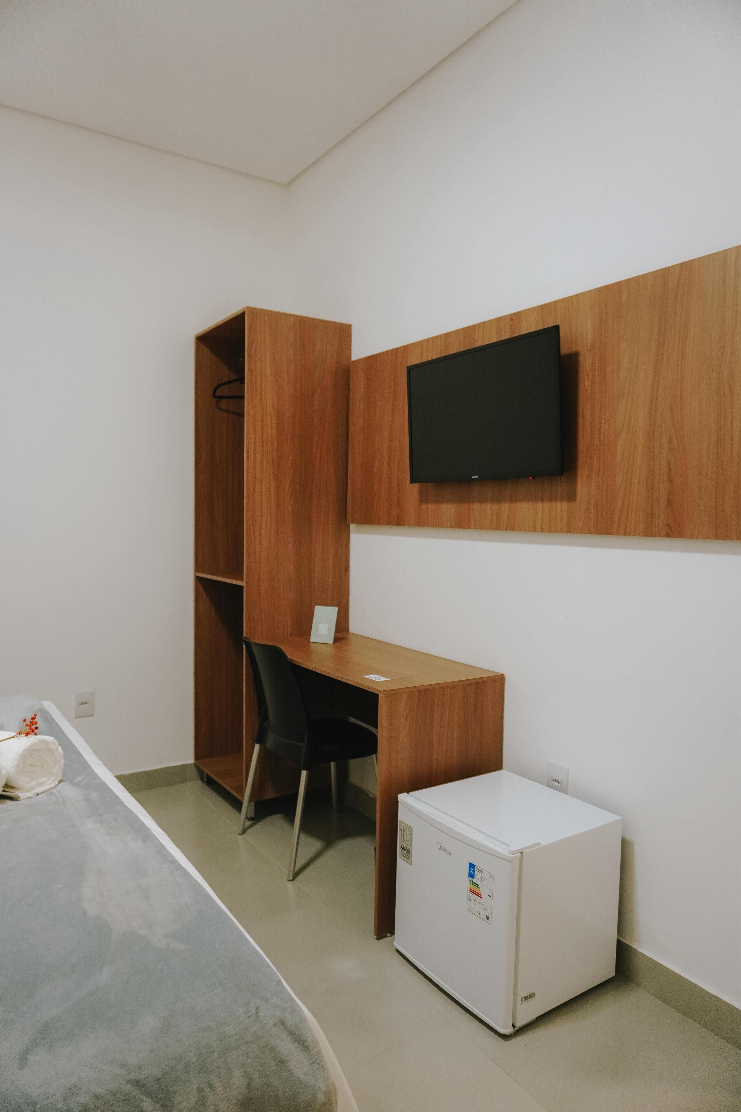 Ein kleiner, moderner Raum mit Schreibtisch aus Holz, einem Stuhl, einem an der Wand befestigten Fernseher und einem kleinen Kühlschrank.