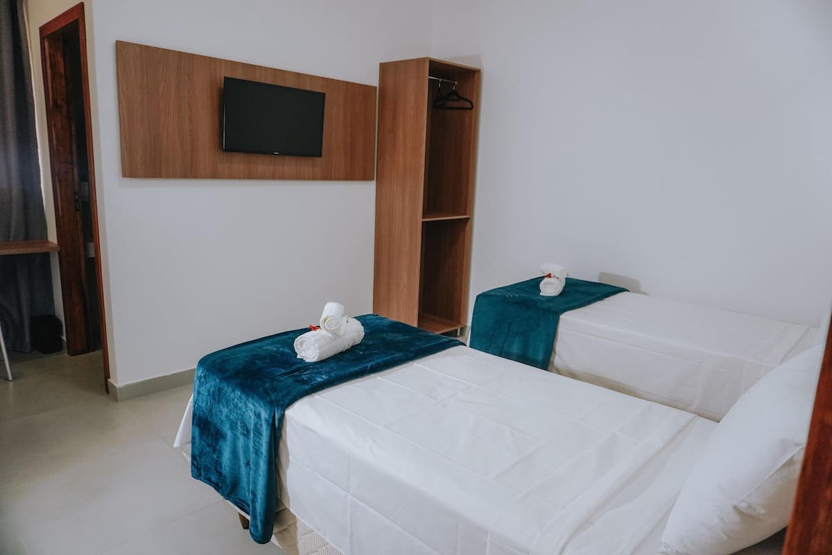 A hotel room with two single beds, a TV mounted on the wall, and a wardrobe.