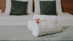 A neatly made bed with white linens, two green pillows, and a white towel with red flowers. - Hotel Villa Garden Janaúba (Janauba)