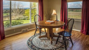 A dining room with a round table, four chairs, a lamp, and a view of a vineyard through large windows. - Historic Vineyard Escape, with patio and vintage charm-Pet friendly! (Dayton)