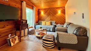 Interior acogedor de una cabaña con techo de madera, una cama grande, un sofá y un televisor.