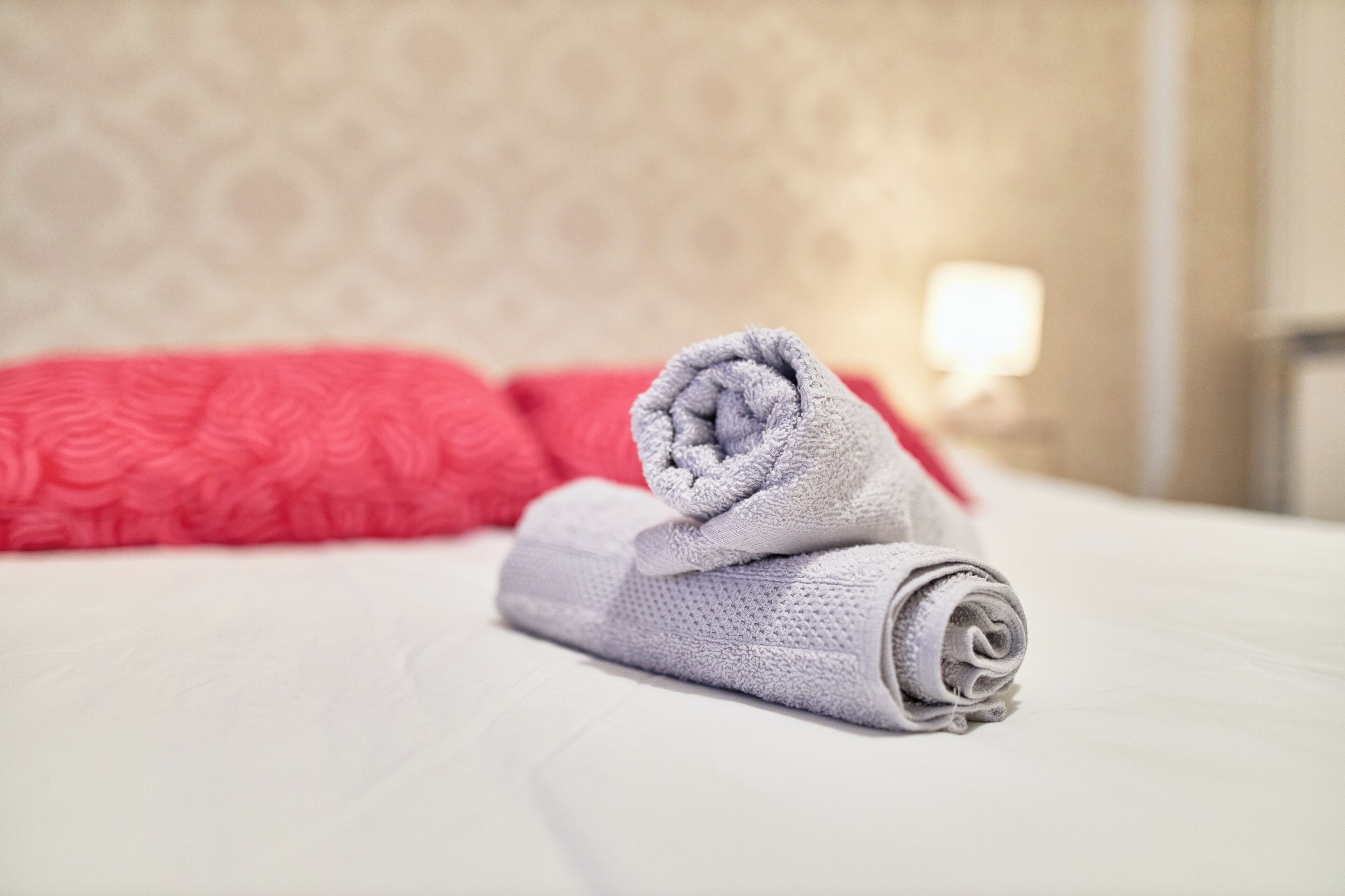 A neatly made bed with a rolled-up towel and a red pillow.