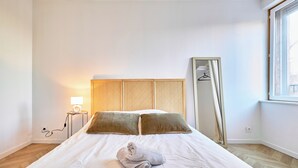 Een net opgemaakt bed met een gevouwen handdoek, een bedlamp en een spiegel aan de muur.