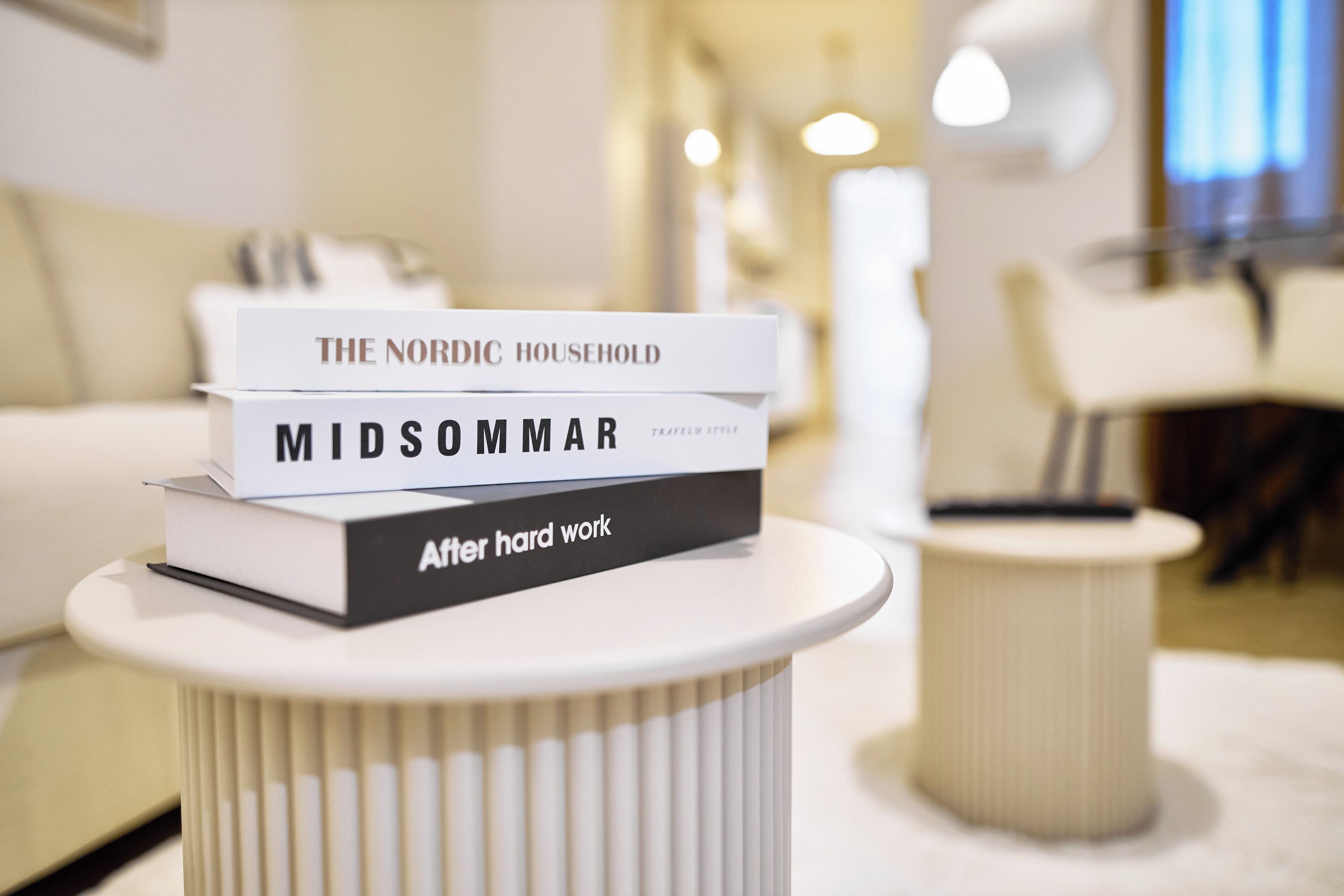 Uma pilha de livros sobre uma mesa branca num quarto moderno, bem iluminado e com design minimalista.