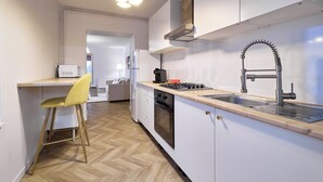 Een moderne keuken met witte kastjes, een houten aanrechtblad, een gele stoel en een inbouwoven.