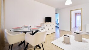 Een moderne eetruimte met een glazen tafel, witte stoelen, een witte kast en een televisie.