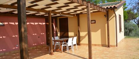 Un espacio cubierto con patio, una mesa y sillas, vigas de madera y piso de baldosas.