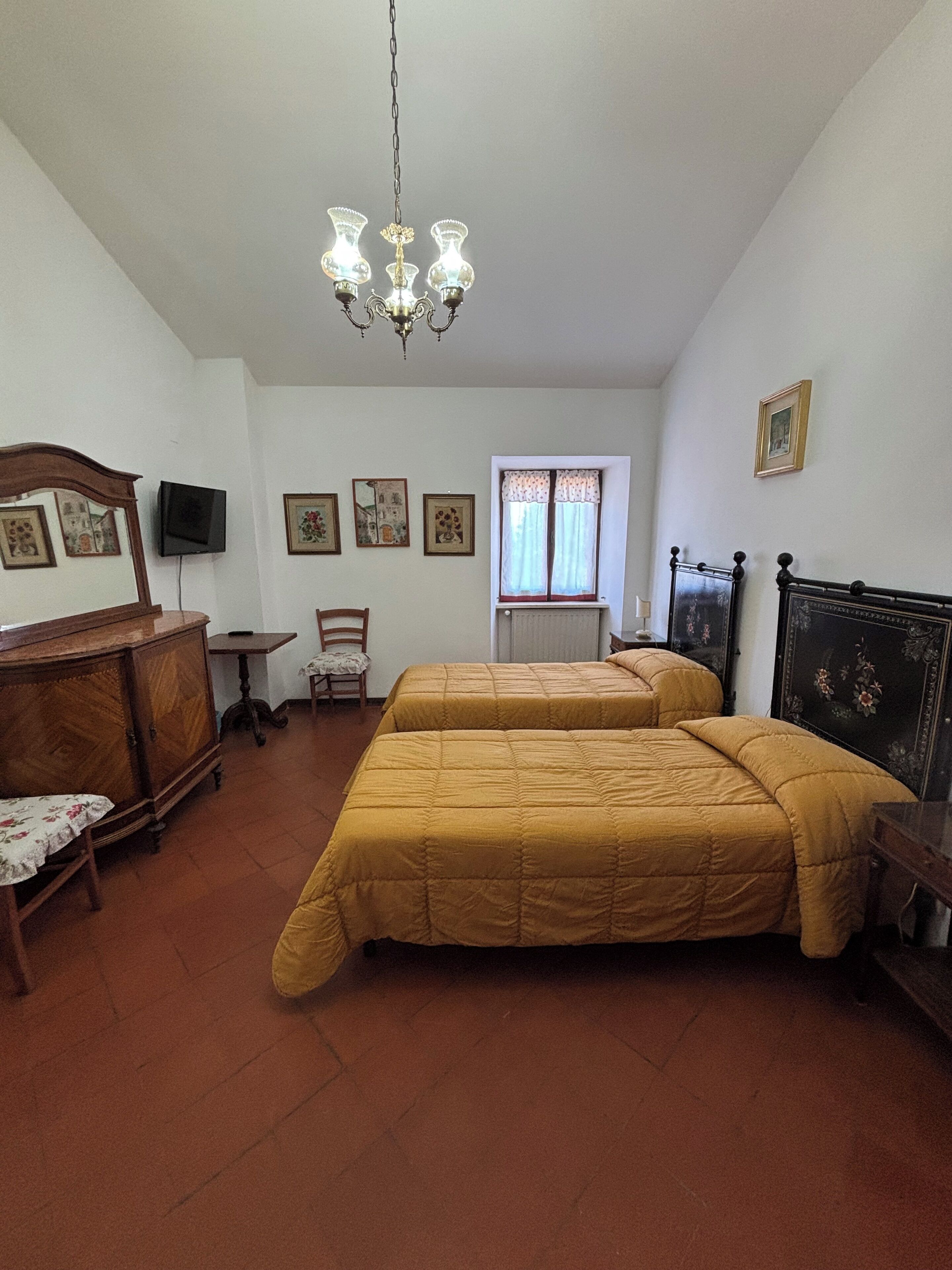 A bedroom with two beds, a wooden dresser, a chair, a television, and a window with curtains.
