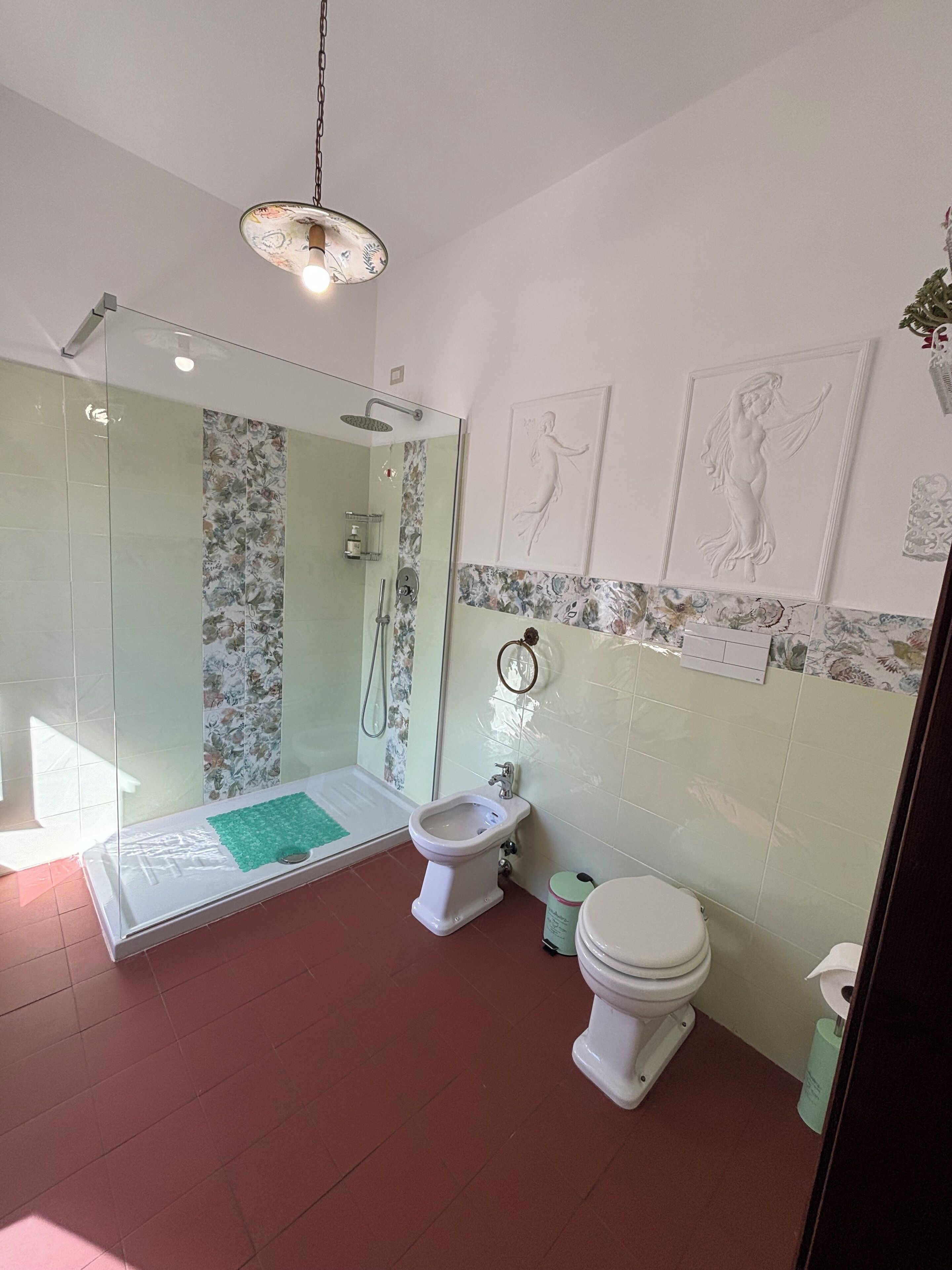 A bathroom with a glass-enclosed shower, a bidet, a toilet, and decorative wall art.