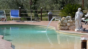 Une piscine agrémentée d’une statue, de chaises longues et d’un élément décoratif en pierre.