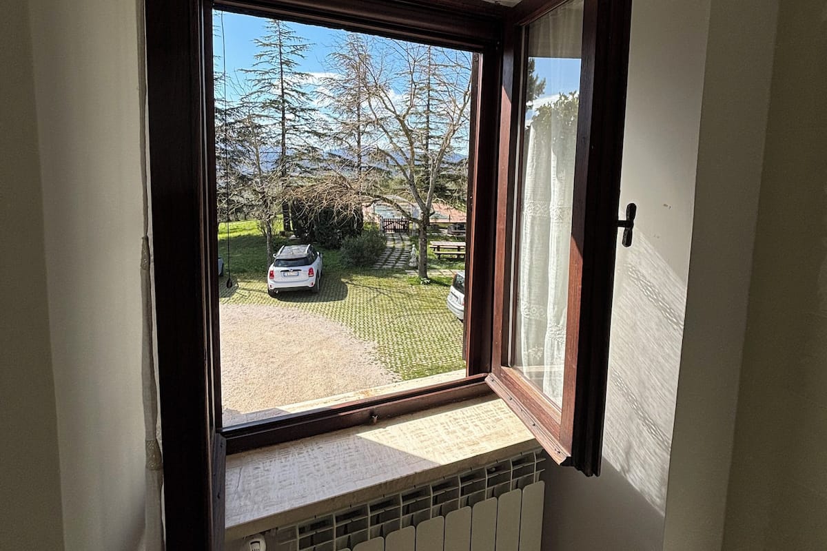 Une pièce avec une fenêtre donnant sur un parking, un radiateur situé sous la fenêtre et une porte sur le côté droit.