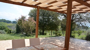 Une terrasse couverte, dotée d’une table et de chaises, qui offre une vue panoramique sur un paysage verdoyant, avec des arbres et les collines à l’horizon.