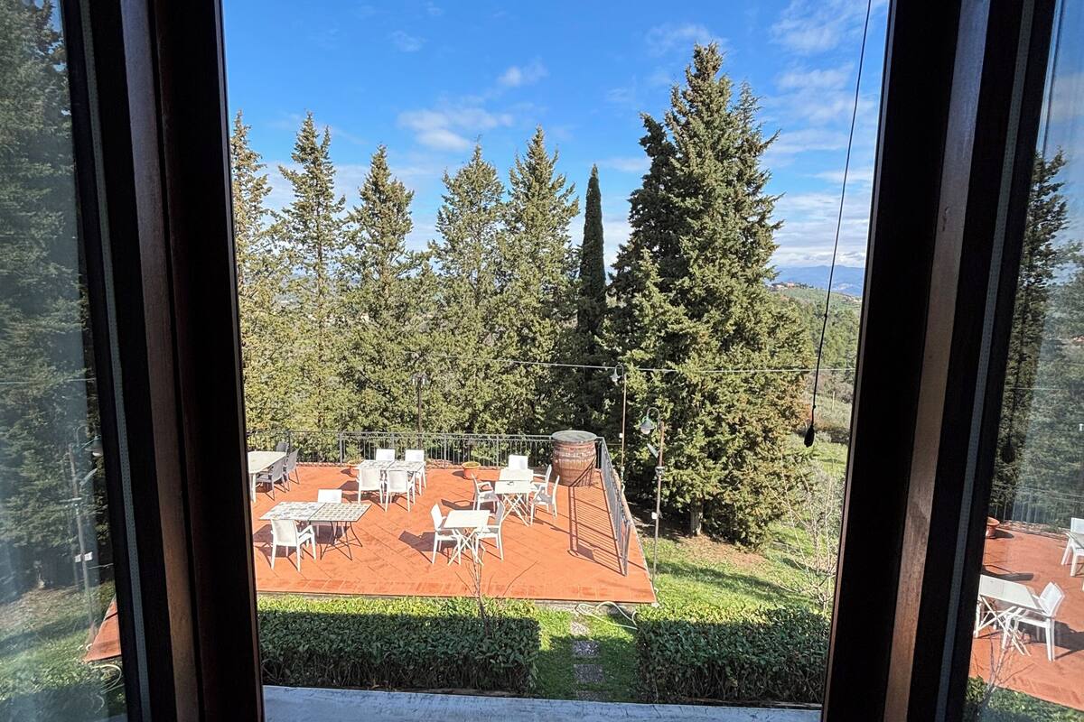 Une vue depuis une fenêtre à cadre en bois, donnant sur un patio aménagé avec du mobilier d’extérieur et une structure surmontée d’un toit rouge.