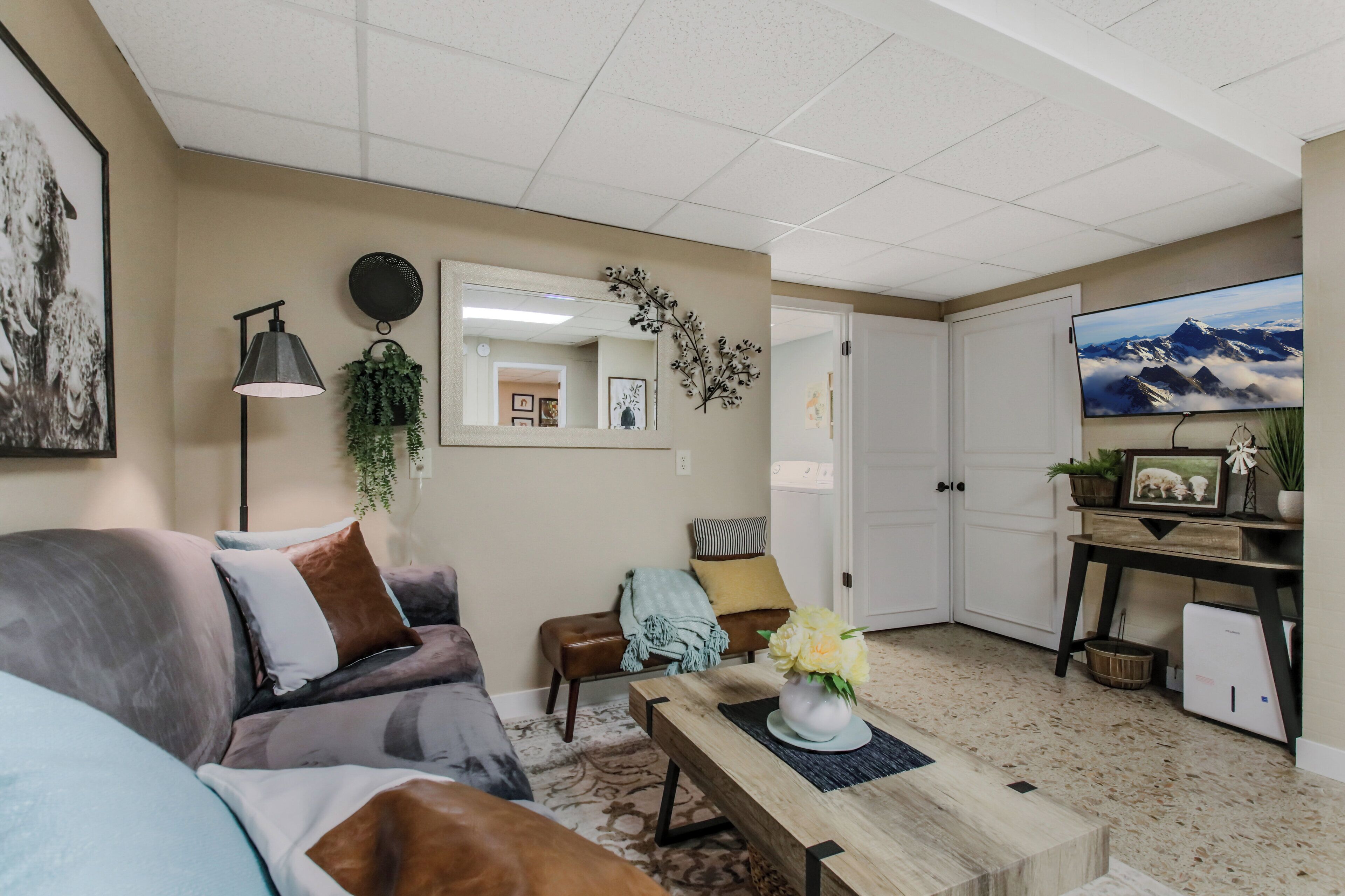 Een woonkamer met een bank, een bijzettafeltje met een vaas, een televisie en een deur naar een andere kamer.