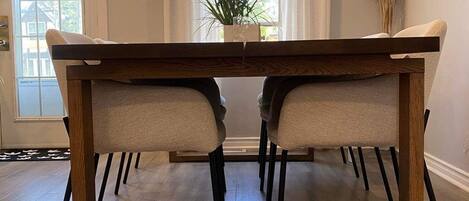 A dining area with a wooden table and chairs, a clock on the wall, and a window with curtains.