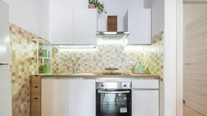 A compact kitchen with white cabinetry, a built-in oven, and a tiled backsplash. - La Casa dei Fiori d'Arancio (Capoterra)