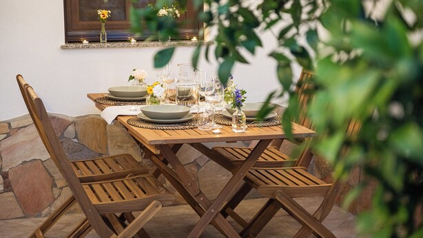 A wooden dining table set with plates, glasses, and a vase of flowers. - La Casa dei Fiori d'Arancio (Capoterra)