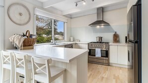 Een moderne keuken met witte kasten, een groot eiland met zitplaatsen, een gasfornuis en een roestvrijstalen afzuigkap.